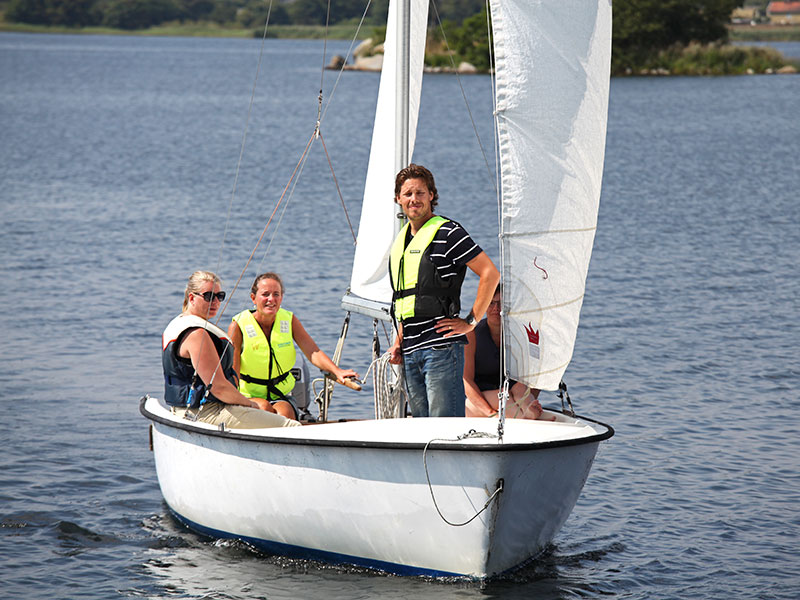 Sommarkurser. Bild på lärare och deltagare i en segelbåt i strålande sol.